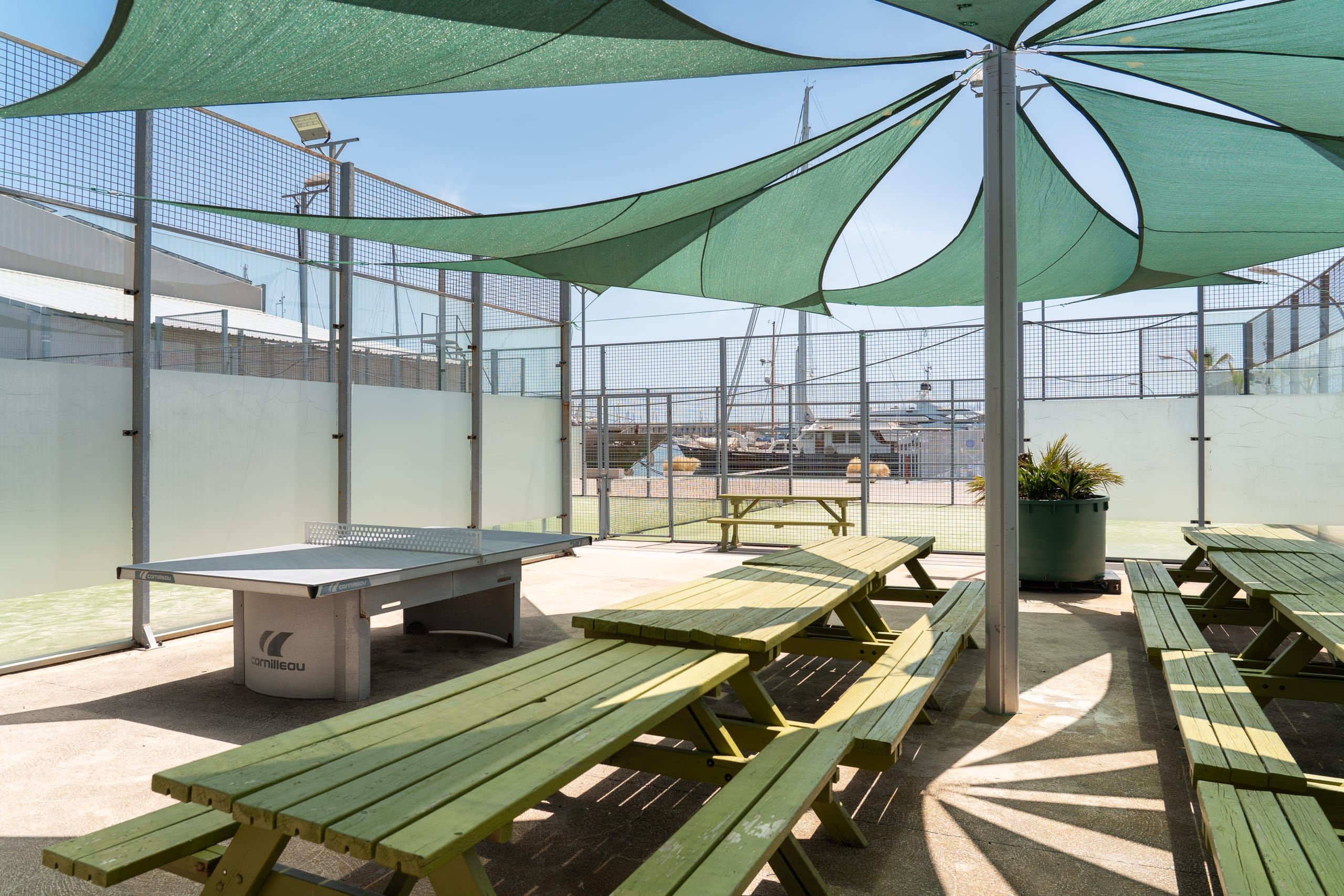 Outdoor terrace of the Crew Club with picnic tables under shade sails and sports courts behind