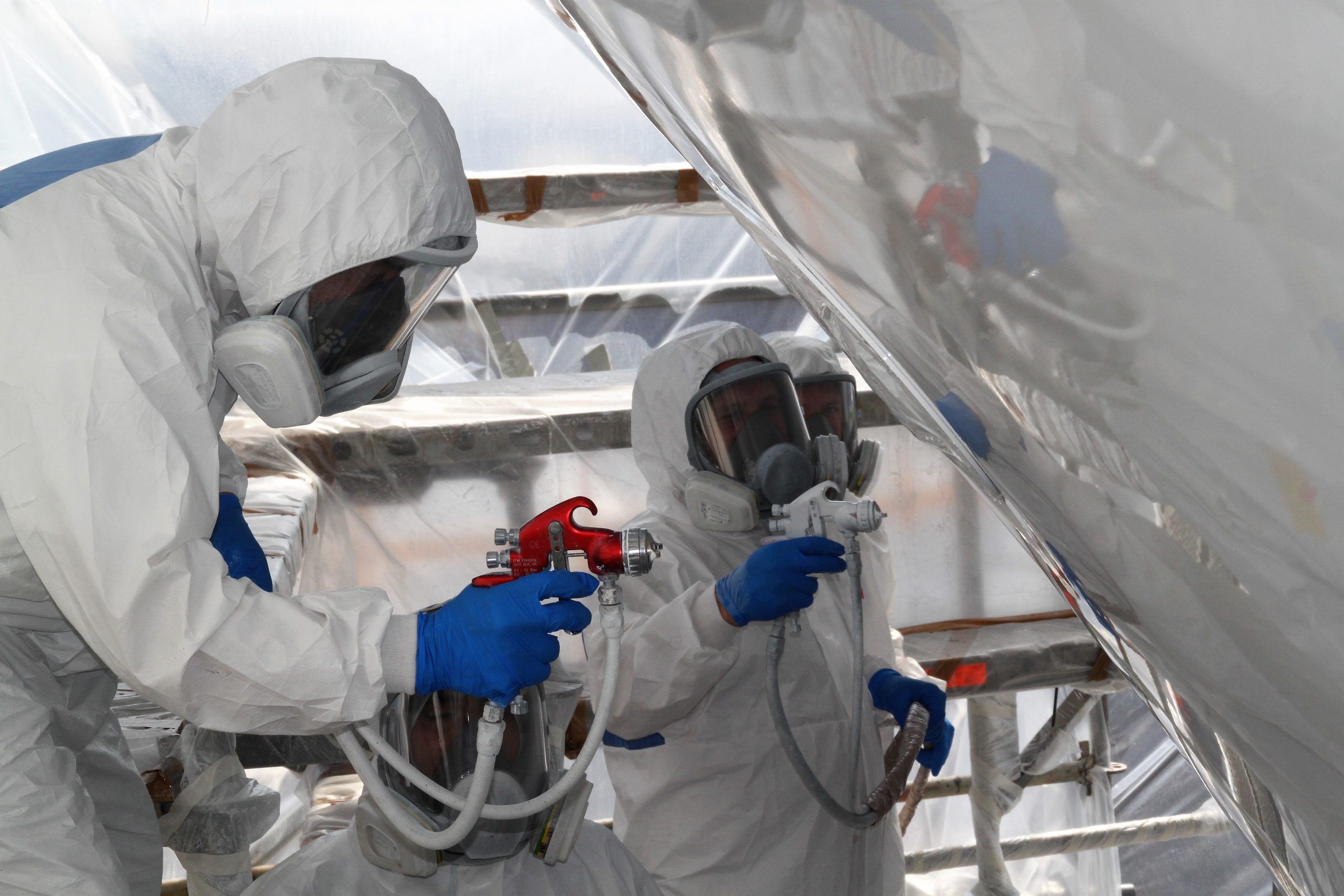 Technicians in protective suits and masks spray-painting a yacht hull